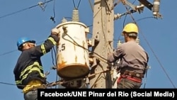 Dos trabajadores de la UNE de Pinar del Río están trabajando en un poste.