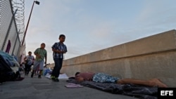 Varias personas que se dirigen a cruzar la frontera pasa delante de varios solicitantes de asilo de Guatemala y Cuba que esperan en un puente a poder entrar en EEUU. (Archivo)